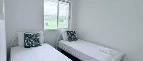 A room with two single beds, a window with a view, and a white ceiling.