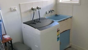 A compact laundry room with a washing machine, a sink, and a small trash bin. - Pet Friendly Coastal Stay Near The Beach. (Bundaberg)