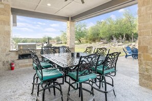 Une terrasse extérieure avec une table et des chaises en métal, un barbecue et une vue sur les arbres et le paysage.