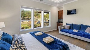 A bedroom with a bed, a sofa, a TV, and a window with a view of the outdoors. - Private 16-Acre Retreat, Pool, Hot Tub & Hill Country Views - Sleeps 16 (Hays County)