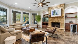 A spacious living room with a fireplace, leather furniture, and a stone accent wall. - Private 16-Acre Retreat, Pool, Hot Tub & Hill Country Views - Sleeps 16 (Hays County)