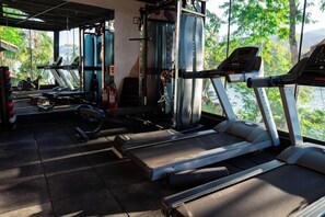 Ein Fitnessstudio mit Laufbändern, Kraftgeräten und Blick auf Grünflächen.
