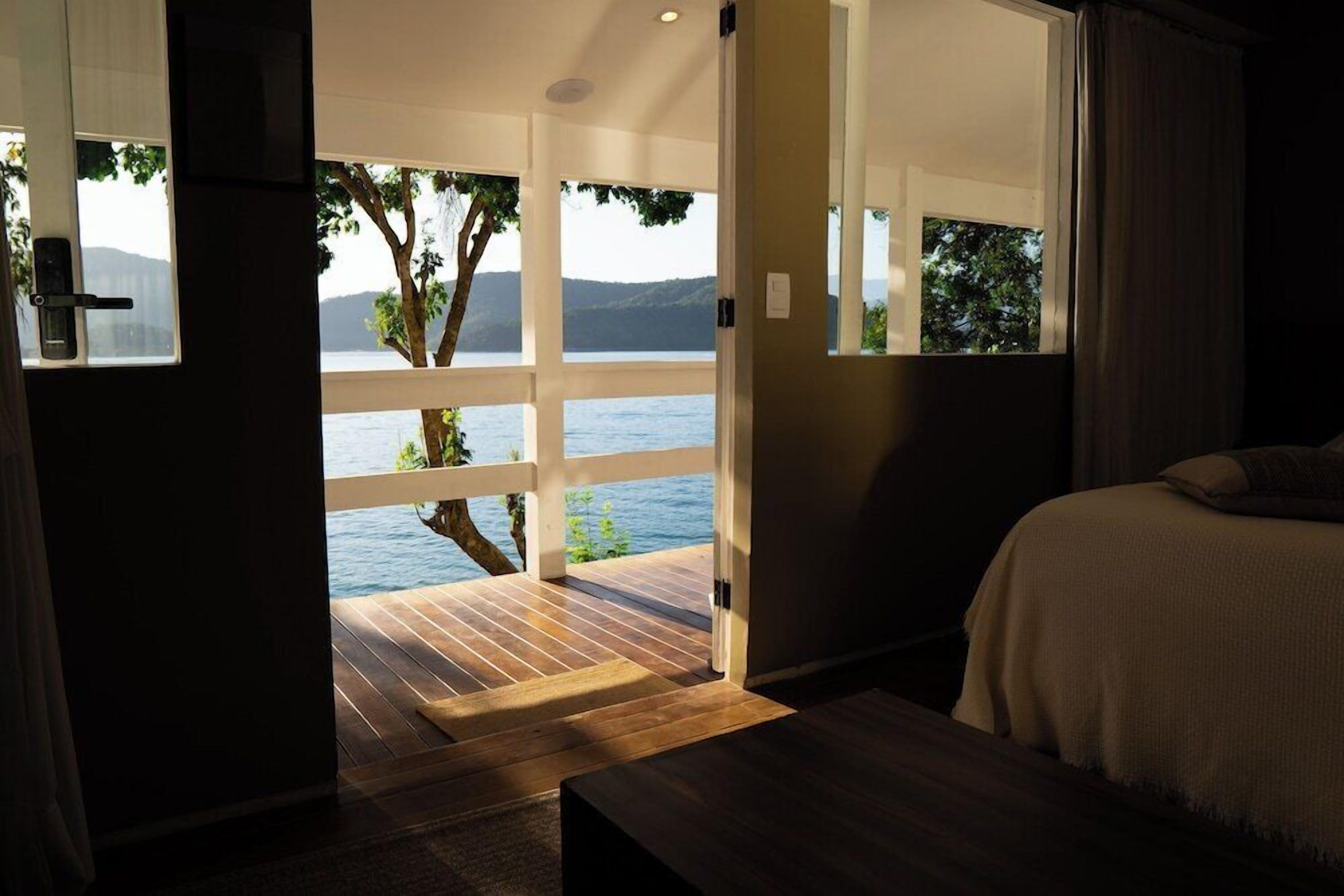 A bedroom with a large window, a wooden floor, and a bed with a white cover.
