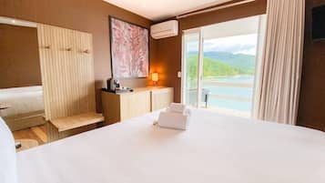 Habitación de hotel con cama, escritorio, silla, lámpara, aire acondicionado y vista a un cuerpo de agua.