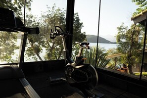 Uma bicicleta ergométrica em um quarto com janelas amplas que dão para um lago e vegetação.