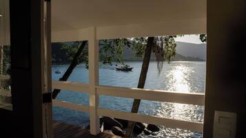Vista desde una habitación con terraza de madera que da a un lago con barcos.