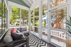 Eine überdachte Veranda mit einer Couch, großen Fenstern und Blick auf die Umgebung.