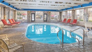 Ein Hallenbad mit Steinböden, roten Liegestühlen und einer weißen Deckenkonstruktion.