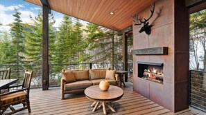 Une terrasse en bois avec un canapé, une table ronde et des chaises, une cheminée et une tête de cerf accrochée au mur.