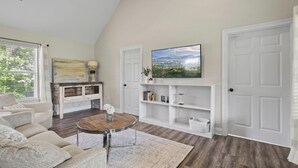 Una sala de estar con sofá, mesa de centro, televisor y estanterías.