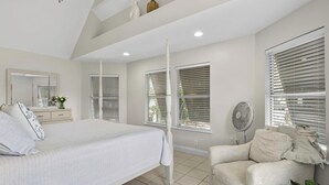 Un dormitorio con cama, una silla, un ventilador y ventanas con persianas.