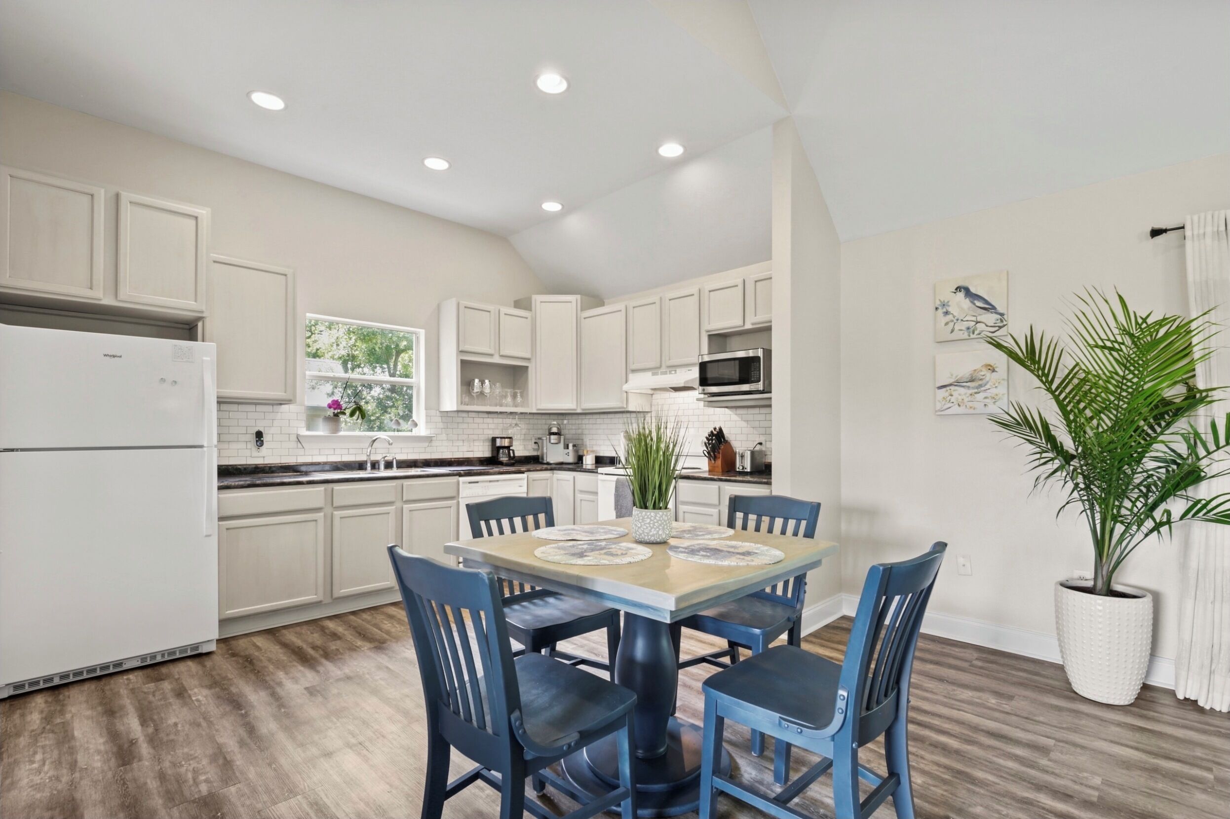 A modern kitchen with white cabinets, a dining table with blue chairs, and a large window.