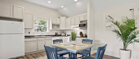 A modern kitchen with white cabinets, a dining table with blue chairs, and a large window.