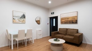A room with a white table and chairs, a brown sofa, and two paintings on the walls. - Central Modern Apartment - Easy Access Location (Auckland Central)