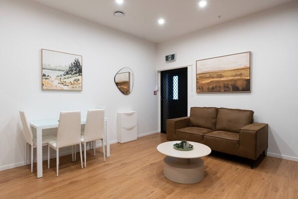 Une pièce avec une table et des chaises blanches, un canapé marron et deux tableaux accrochés aux murs.