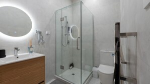 A modern bathroom with a glass-enclosed shower, a round mirror, a white sink, and a toilet. - Central Modern Apartment - Easy Access Location (Auckland Central)