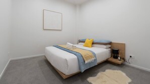 A bedroom with a bed, bedside table, lamp, and a framed picture on the wall. - Central Modern Apartment - Easy Access Location (Auckland Central)