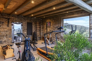 Un gimnasio de paredes de piedra con equipamiento de ejercicio, una cinta de correr y vistas al exterior.