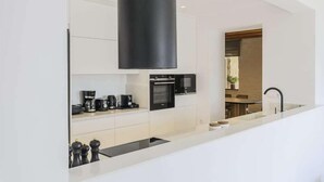 A modern kitchen with white cabinetry, a black range hood, a built-in oven, and a coffee station. - Nasta Intentional Living Mykonos (Mykonos)