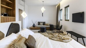 A modern hotel room with a bed, a seating area, a TV, and a wooden shelf. - Nasta Intentional Living Mykonos (Mykonos)