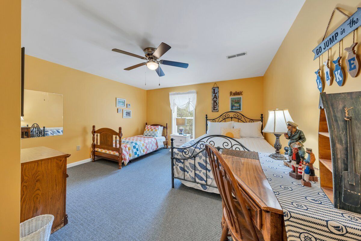 A bedroom with two beds, a ceiling fan, a dresser, a desk, and a wall with a 'GO JUMP IN the LAKE' sign.