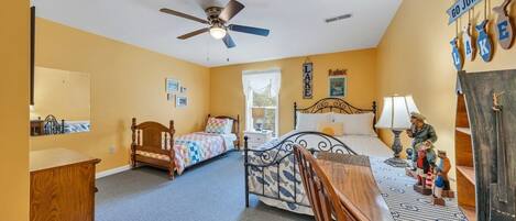 A bedroom with two beds, a ceiling fan, a dresser, a desk, and a wall with a 'GO JUMP IN the LAKE' sign.