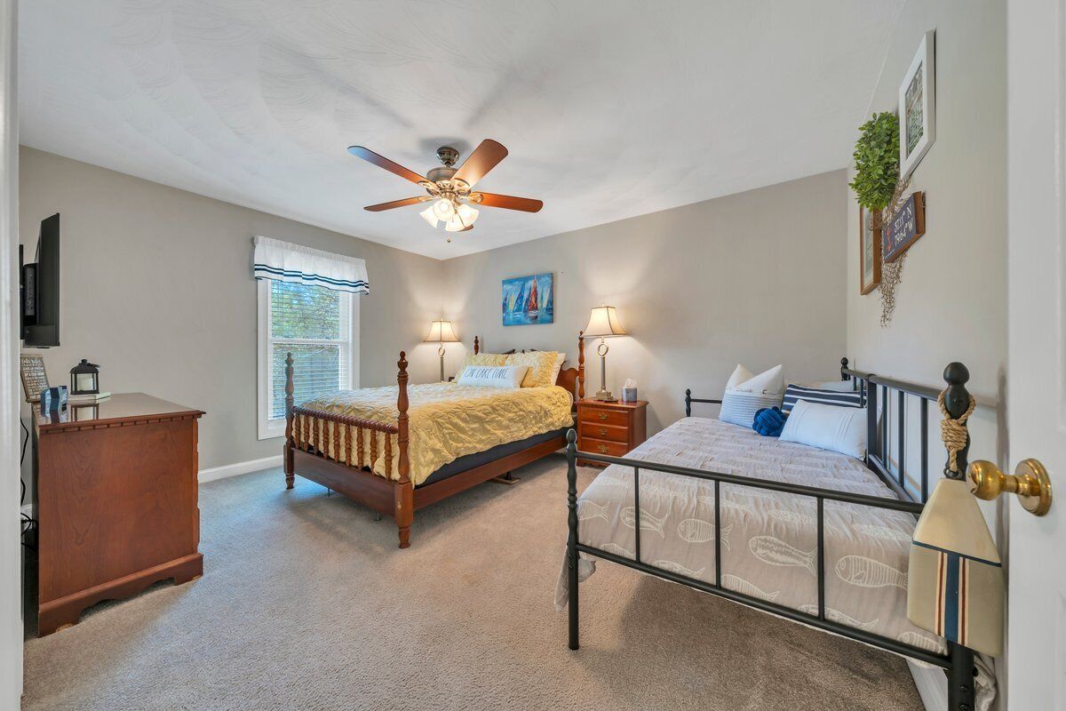 A bedroom with a bed, a nightstand, a dresser, a ceiling fan, and a window.