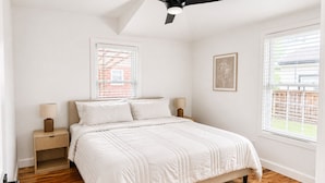 Une chambre à coucher comprenant un lit, deux tables de chevet, un ventilateur de plafond et deux fenêtres.