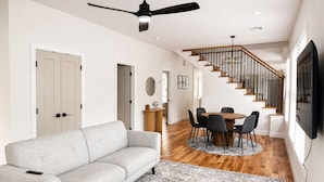 Un salon moderne avec un canapé gris, une table à manger avec des chaises, un escalier et un téléviseur à écran plat fixé au mur.