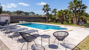 Ein Swimmingpool mit Liegestühlen und Tischen, umgeben von Palmen.