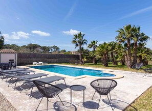 Ein Swimmingpool mit Liegestühlen und Tischen, umgeben von Palmen.
