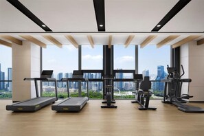 Ein Fitnessstudio mit Laufbändern, Crosstrainern und Krafttrainingsgeräten, große Fenster mit Blick auf die Stadt.
