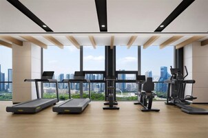 Un gimnasio con cintas de correr, elípticas y equipo de pesas, amplias ventanas con vista a la ciudad.