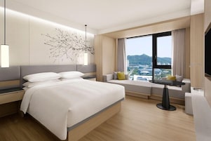 Una habitación de hotel moderna con una cama grande, un sofá, una mesa de comedor y un ventanal con vistas a la ciudad.