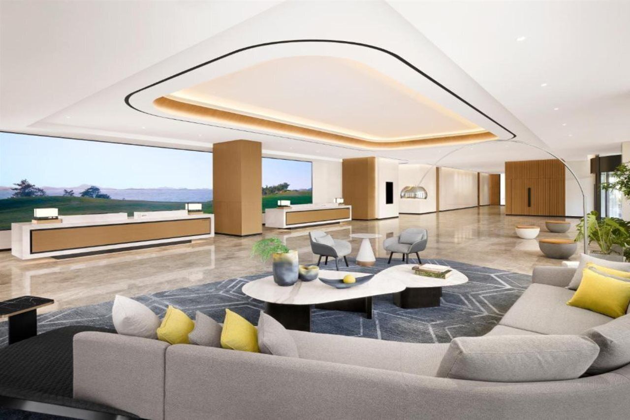 A modern hotel lobby with a reception desk, seating area, and large windows offering a view of the outdoors.
