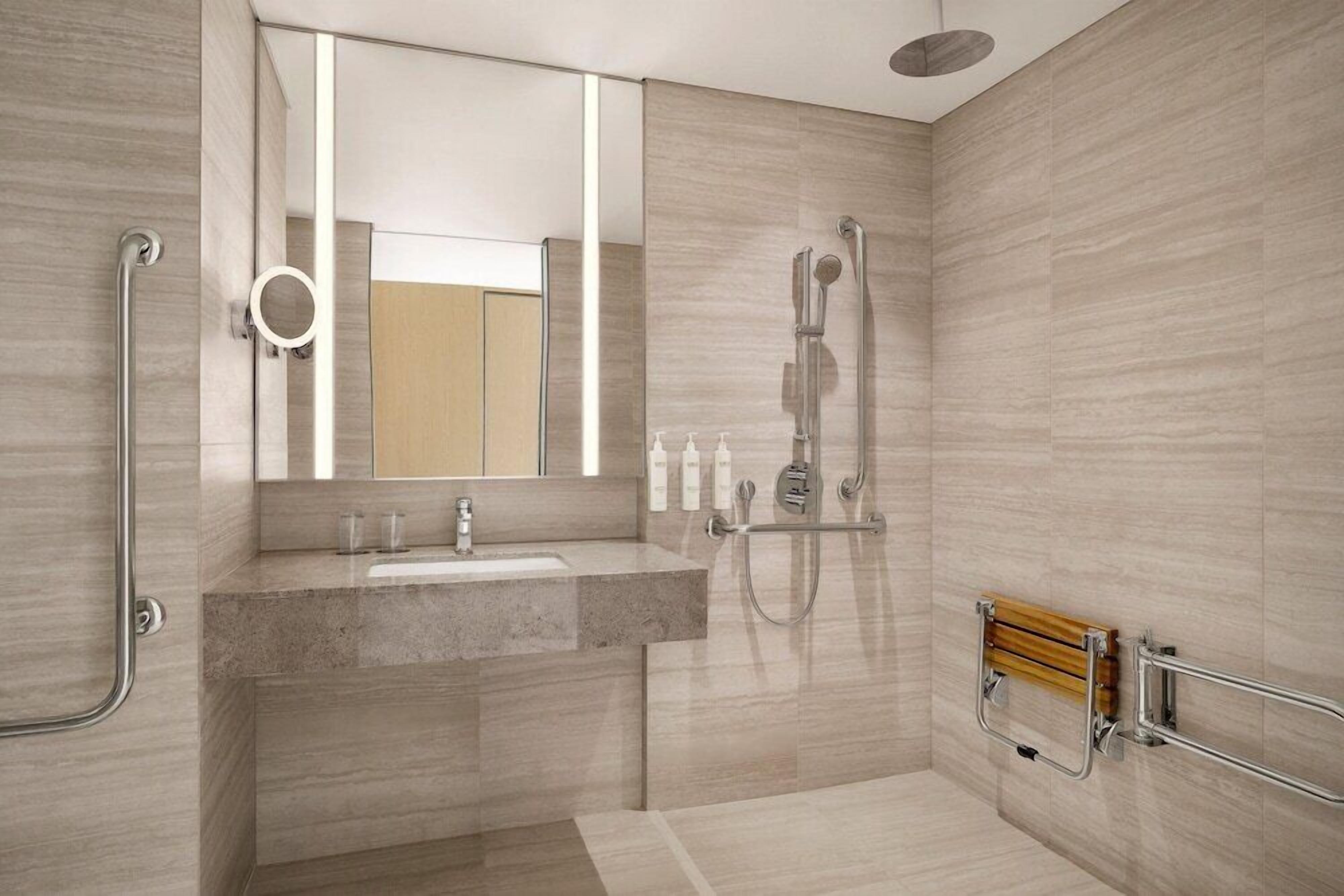 Un baño moderno con lavamanos, espejo, ducha y barras de apoyo.