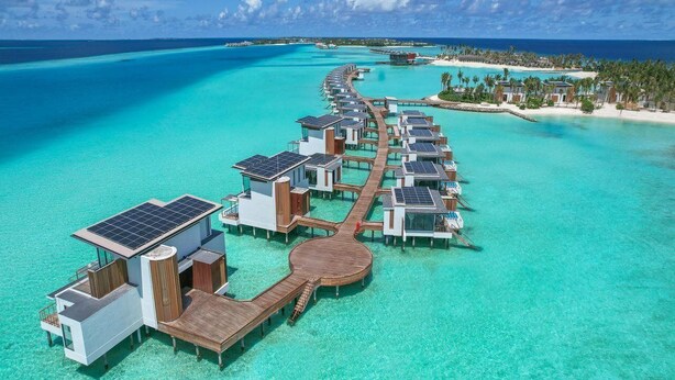 Un resort sobre el agua con bungalows individuales conectados por pasarelas, paneles solares y aguas turquesas cristalinas.