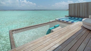 Una terraza de madera con piscina y zona de descanso con vistas a aguas turquesas.