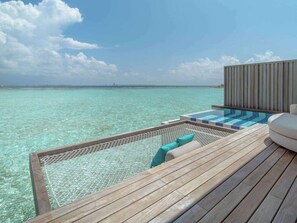 Um deck de madeira com piscina e área de estar com vista para águas turquesa.