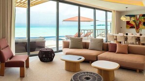 Habitación de hotel moderna con un gran ventanal que ofrece vista al mar, un sofá, dos mesitas de centro y una silla.