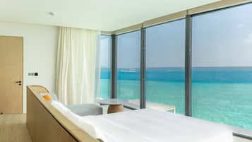 Habitación de hotel con cama, una mesita, una silla y vista al océano.