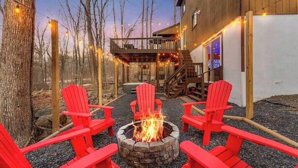 Una cabaña con un brasero, sillas Adirondack rojas y luces colgantes.