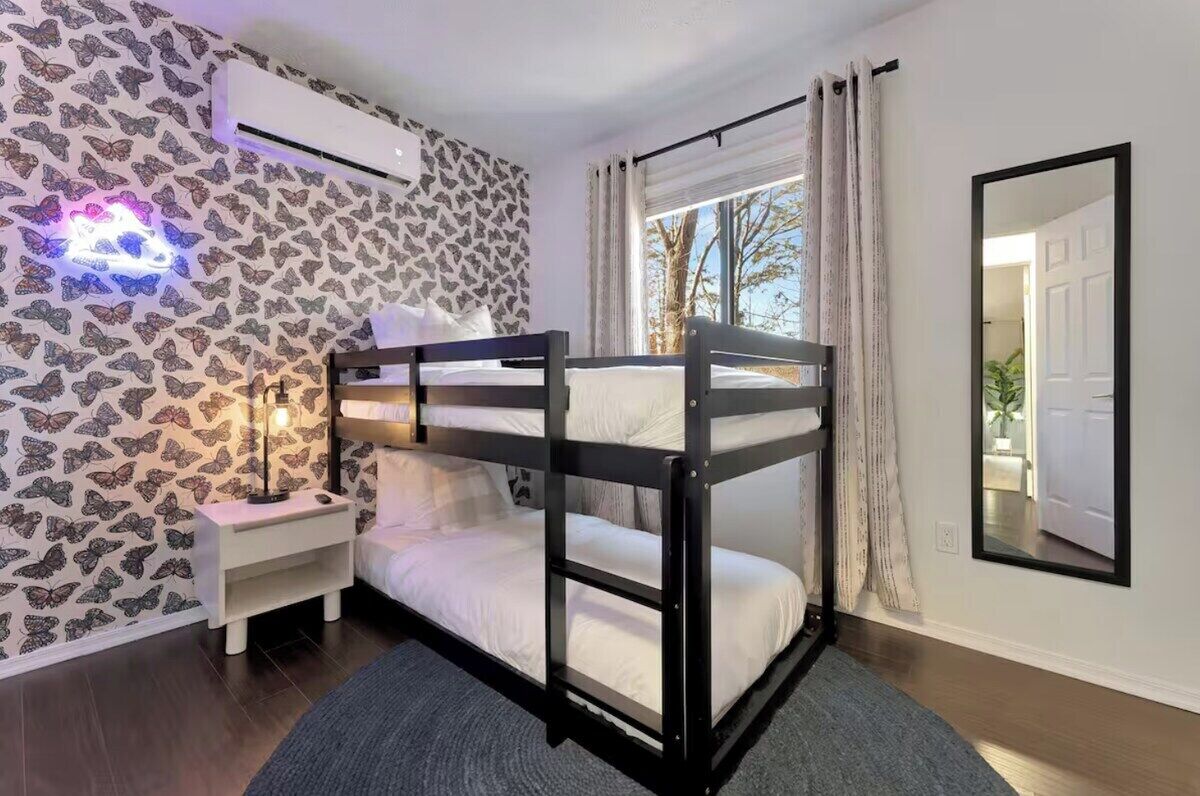 A bunk bed room with a patterned wall, a bedside table, a nightstand, and a window with curtains.