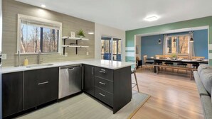 Una cocina moderna con muebles oscuros, lavavajillas y un comedor con mesa y sillas.