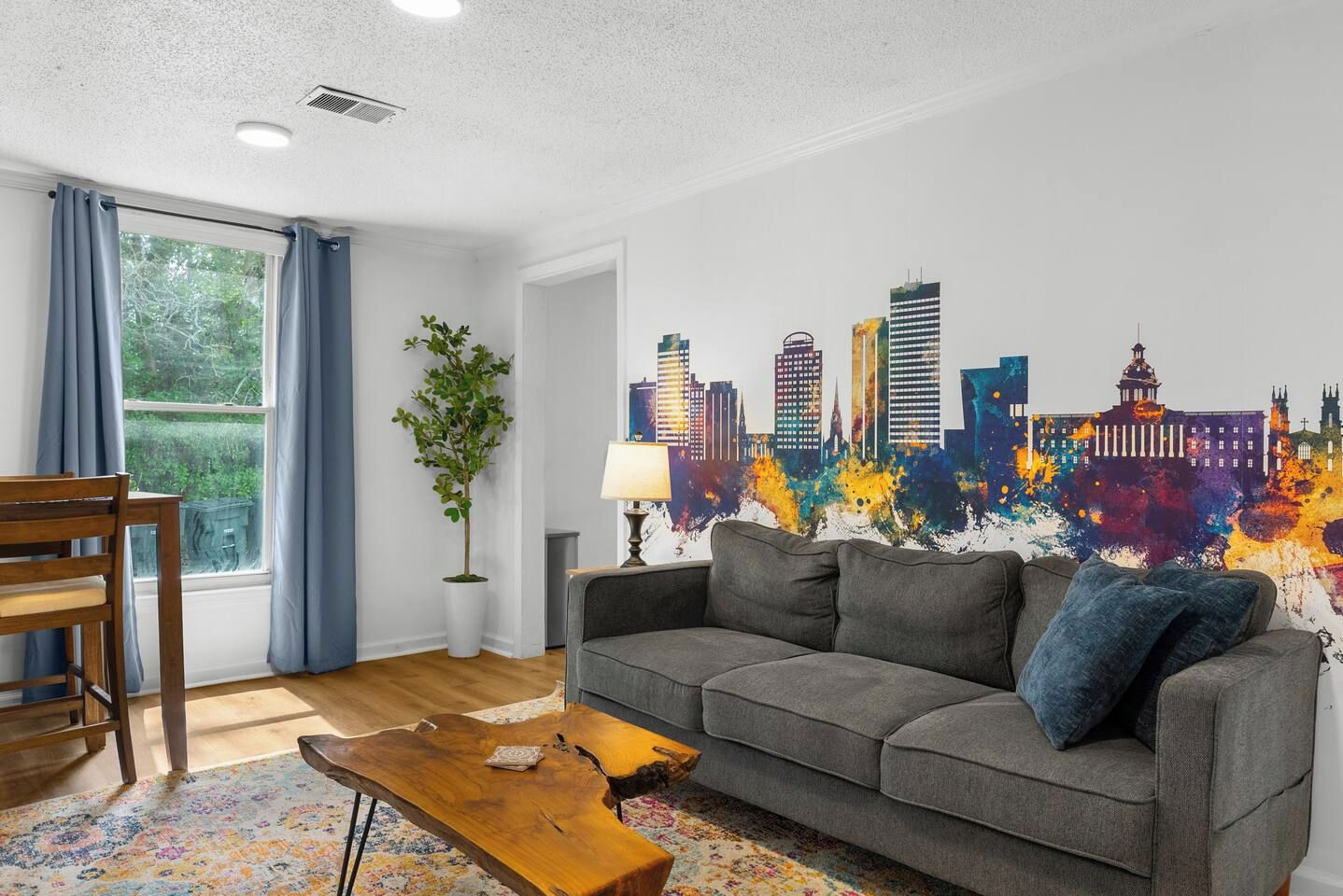 A modern living room with a grey sofa, wooden coffee table, and a cityscape mural on the wall.