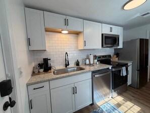 A compact kitchen with white cabinets, a stainless steel sink, a microwave, a stove, and a refrigerator. - 2BR Bungalow | Fire Pit + Near 5 Points + Prisma (Columbia)