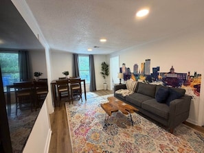 A living room with a sofa, coffee table, and a cityscape mural on the wall. - 2BR Bungalow | Fire Pit + Near 5 Points + Prisma (Columbia)