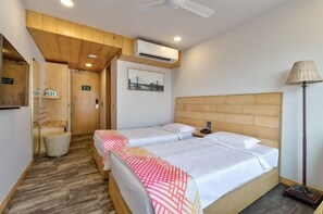 A hotel room with two beds, a wooden ceiling, an air conditioning unit, a lamp, and a framed picture on the wall. - Ginger Surat (Surat)