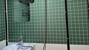 Une salle de bain avec des murs recouverts de carreaux verts, un lavabo blanc, une douchette à main et un luminaire au plafond.
