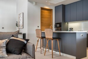 Een moderne keuken met donkere kastjes, een houten deur en een klein eiland met twee stoelen.